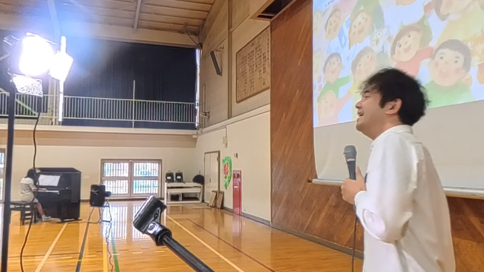 しあわせになあれを歌う様子とピアノ伴奏の児童の後ろ姿